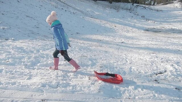 A girl pulling a sledge up a snowy hill for some wintertime fun