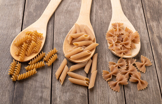 Assorted whole wheat pasta on spoons over wooden table