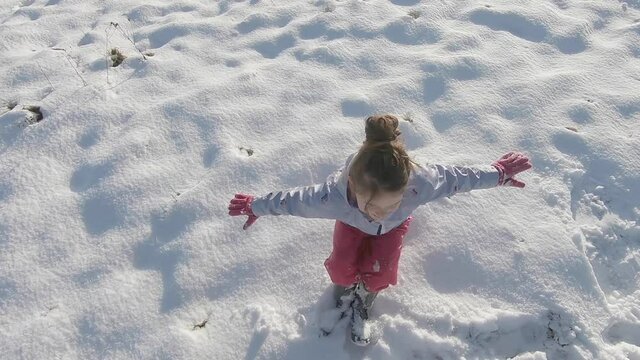A young girl falling backwards in the fresh snow and making a snow angel with her arms and legs