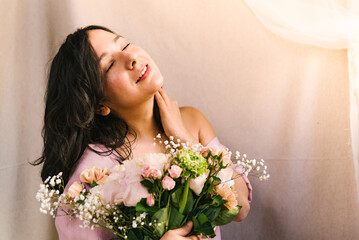Obraz na płótnie Canvas attractive young woman enjoying and feeling the sun holding a flowers bouquet with simple pink dress. Smiling and confident woman during spring.