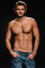 Fototapeta premium muscular confident man posing with hands in pockets while looking at camera on black background