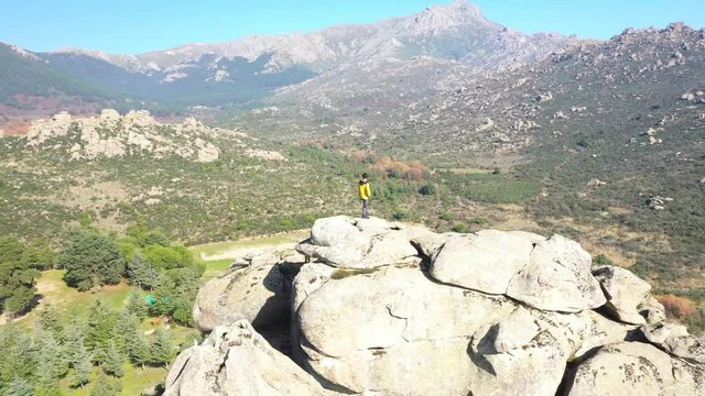 Young man perched on some rocks looking at the horizon in a natural park seen from a drone