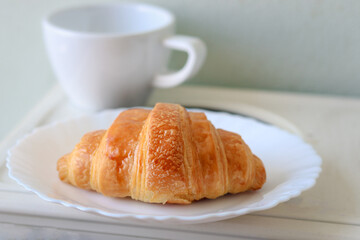 Croissant on white plate with coffee on the breakfast table in the morning, dessert at tea time break to relax