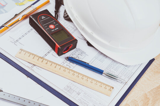 helmet and tools for construction drawings and construction drawings and laser rangefinder for distance measurements, close-up, selective focus, tinted image,