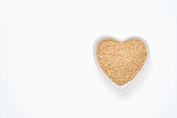 Quinoa grains in bowl of the shape of heart isolated on white background, top view