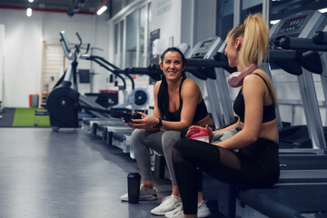 Fit young woman sitting and resting after workout or exercise in fitness gym