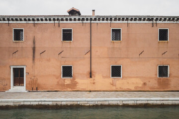 Wall with windows and door by road next to canal in Venice, Italy