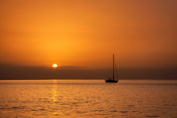 Sailing boat anchored at sea drenched in a golden sunset with sun just above horizon