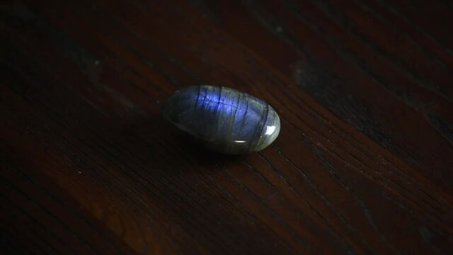 Close up view of gemstone labradorite ( Labradorescence) spinning on brown wooden background.  Labradorescence in labdradorite, visible as the angle of view changes.