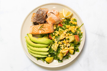 Healthy salad with avocado, corn, salmon fillet and crispy salmon skin on plate isolated on white background. 