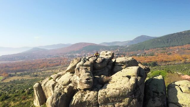 Young man perched on some rocks looking at the horizon in a natural park seen from a drone