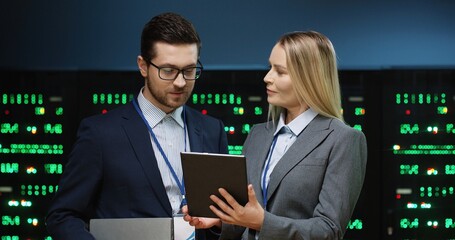 Chief female programmer standing in server room holding tablet explaining problem in system support...