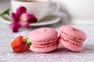 Strawberry macaroon (macaron) closeup on white table background. Sweet tasty pink macaroon and cup of coffee for breakfast dessert. French cookies macaroons - cute cake of meringue almond biscuit