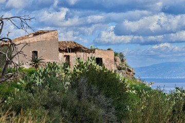 Fototapeta premium abandoned rural house on the coast of Eastern Sicily in the Province of Messina built on a promontory overlooking the sea with typical Mediterranean vegetation and succulents