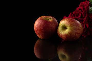 Fototapeta na wymiar Apples, beautiful red apples with a bouquet of red roses on reflective surface, black background, selective focus.