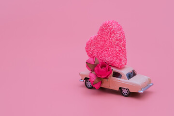 Toy retro car with flowers carrying big heart. Romantic love and Valentine's day concept. Copy space