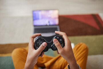 Close up of unrecognizable African-American boy playing videogames at home with focus on hands holding gamepad, copy space