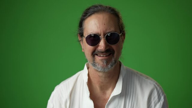 Portrait of smiling mature handsome man wearing sunglasses on a green screen chroma key background.