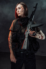 Seductive female soldier with tattoo and bandaged hand poses in dark foggy background holding rifle on her shoulder.