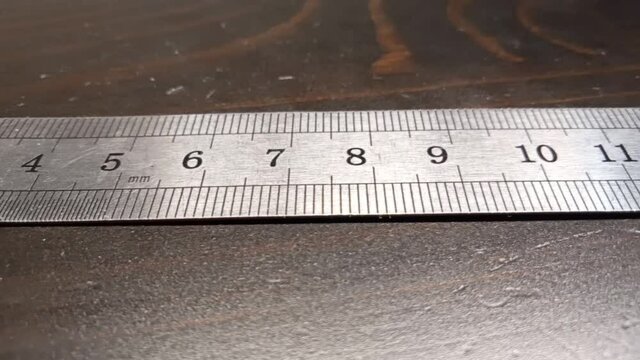 Pan along a metal ruler. Metal ruler on a wooden background.