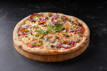 Pizza with meat cheese onion jalapeno on a dark background.