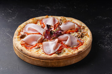 Pizza with cheese, meat, red bell pepper, lettuce leaves and ham on a dark background.