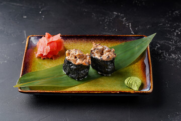 Gunkans with eel fish on a plate are decorated with bamboo leaf wasabi and ginger on a dark background.