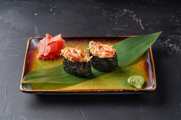 Gunkans sushi with a crab on a dark background. Decorated with bamboo leaf, ginger and wasabi.