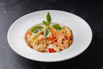 Pasta with big shrimp on a dark background. In a white deep dish.