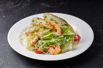 Caesar salad with shrimp on a white plate on a dark background.