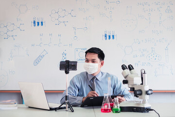 Science chemistry teacher wearing mask and   teaching online with smartphone in the classroom