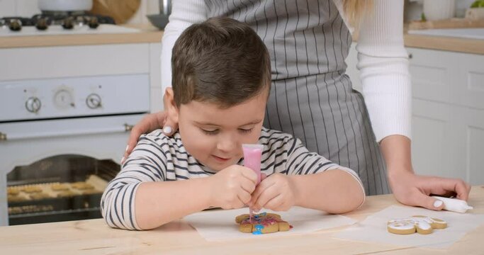 Focused little boy decorating homemade gingerbread cookie with colorful icing ay kitchen, close up, slow motion