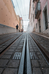Fototapeta na wymiar Photograph of a runner from the back, jogging on a steep street in Lisbon, where the tram rails that run through the city can be seen on the ground.