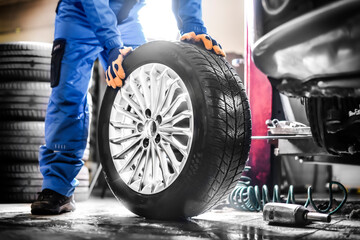 Auto mechanic working in garage and changing wheel alloy tire. - obrazy, fototapety, plakaty