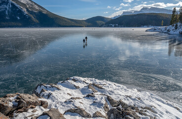 Fototapeta premium Two ice skaters on Lake Minnewanka in Banff National Park, Alberta, Canada