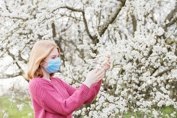 Happy teenager girl in medical mask in spring flowering garden. Concept of social distance and prevention of coronavirus.