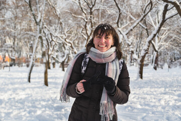 Fototapeta na wymiar Happy young woman after playing with snow in a snow-covered winter park. Girl enjoying snowy winter, frosty day. Walk in winter forest