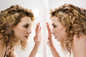 Face in profile with curly blond hair trying to see something thru the mirror