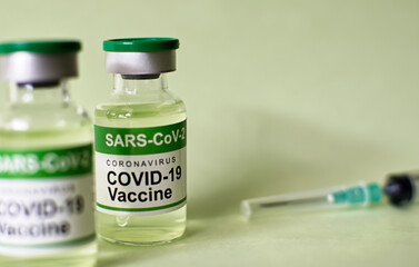 COVID-19 coronavirus vaccine bottle on green background