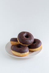 A pile of chocolate donuts on a white plate with copy space
