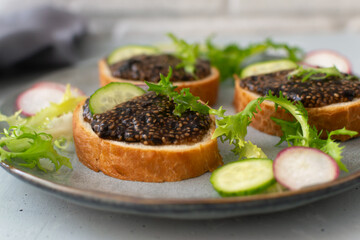 Chia seed appetizer on pieces of baguette with cucumber and radish on a gray plate on a gray background. Copy space. Horizontal orientation.