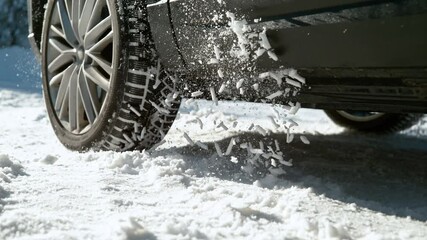 SLOW MOTION, LOW ANGLE, CLOSE UP, DOF: Car's wheels spin in place and spew up pieces of white snow as it attempts to gain traction on the slippery road. Snow flies up from a vehicle's spinning wheel.