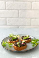 Three chia seed sandwiches on baguette pieces with vegetables and herbs on a gray plate on a gray background. Copy space. Vertical orientation.