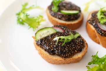 Chia seed sandwiches on baguette pieces with cucumber, radish and herbs on a white plate. Vegan food concept. Copy space. Close-up. Horizontal orientation.