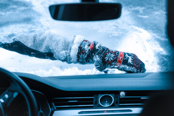 Close up of woman hand with Christmas winter glove. Cleaning snow on car windshield. View from inside of car.
