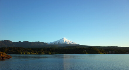 Nature of Chile, Beautiful panoramic landscape, lake Villarrica and snow capped Villarrica volcano under blue sky evning light. Pucon