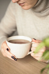 Woman in beige sweater holding a cup of tea. Selective focus.