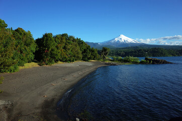 Nature of Chile, Beautiful landscape, Dark volcanic sand beach on Villarrica lake, snow capped Villarrica volcano under blue sky in sunny day. Green environment, Pucon