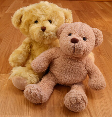 Two cute stuffed teddy bears. Softly smiling kindly. Close up and isolated against a wooden background.