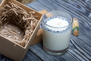 Decorative candle in craft packaging. Tied with a cord and decorated with lavender branches. Nearby is a bottle of matches.